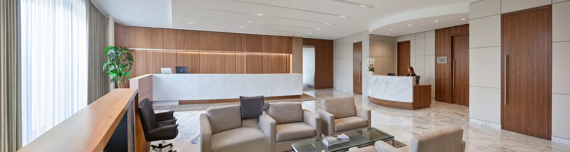 Hotel reception area with marble-front desk, wood-paneled walls, and plush beige seating in a bright lobby